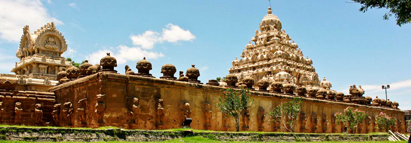 Wide dusk view of an old stone building complex with a tiered tower, warm amber sky and green lawns in the foreground